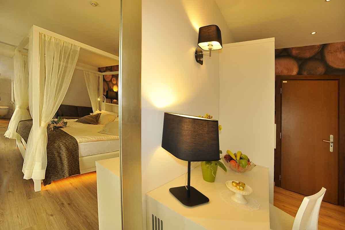 A bedroom with a canopy bed, a bedside table with a lamp, and a fruit bowl.
