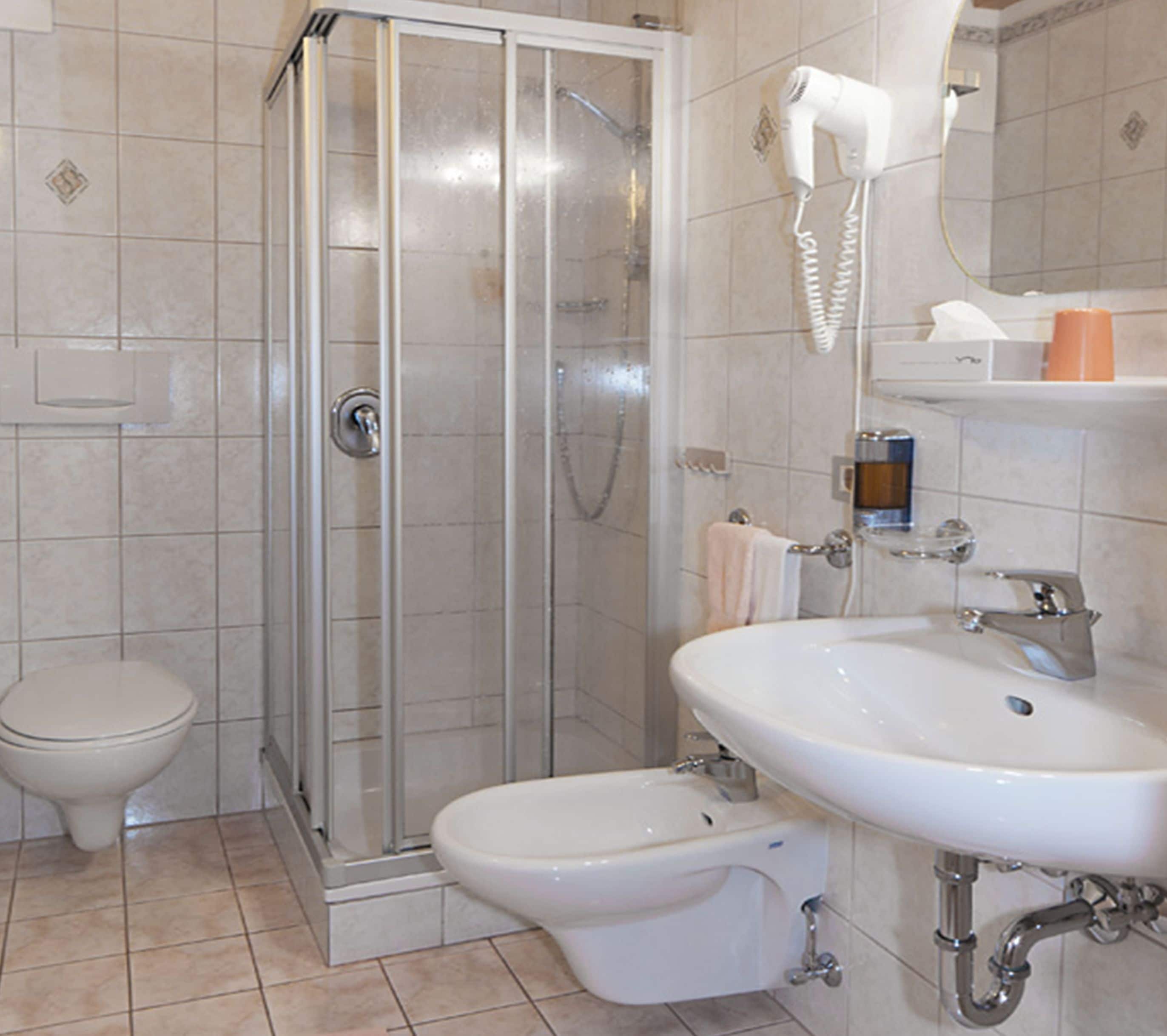 A bathroom with a glass-enclosed shower, a toilet, a bidet, and a sink with a mirror above.