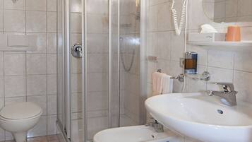 A bathroom with a glass-enclosed shower, a toilet, a bidet, and a sink with a mirror above.