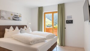 A bedroom with a bed, pillows, a painting, a window with curtains, and a wall-mounted control panel. - Residence Töglhof (Funes)