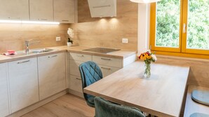 A modern kitchen with wooden cabinets, a stainless steel sink, and a dining area with a table and chairs. - Residence Töglhof (Funes)