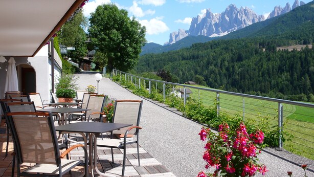 An outdoor terrace with tables and chairs, overlooking a mountainous landscape. - Residence Töglhof (Funes)