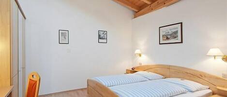 A bedroom with a wooden bed, a wooden chair, and a nightstand with a lamp.