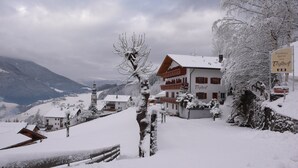 A snow-covered mountain village with traditional wooden buildings, a clock tower, and a sign for 'Residence Garní Töglhof'. - Residence Töglhof (Funes)