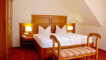 A hotel room with a wooden bed, two bedside tables with lamps, a wooden bench, and a red patterned carpet.