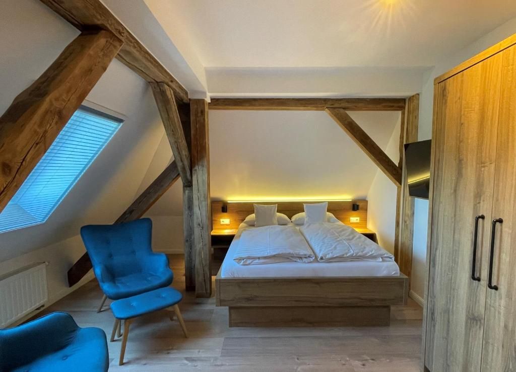 Une chambre avec un plafond en pente, un lit, une chaise bleue et des poutres en bois.