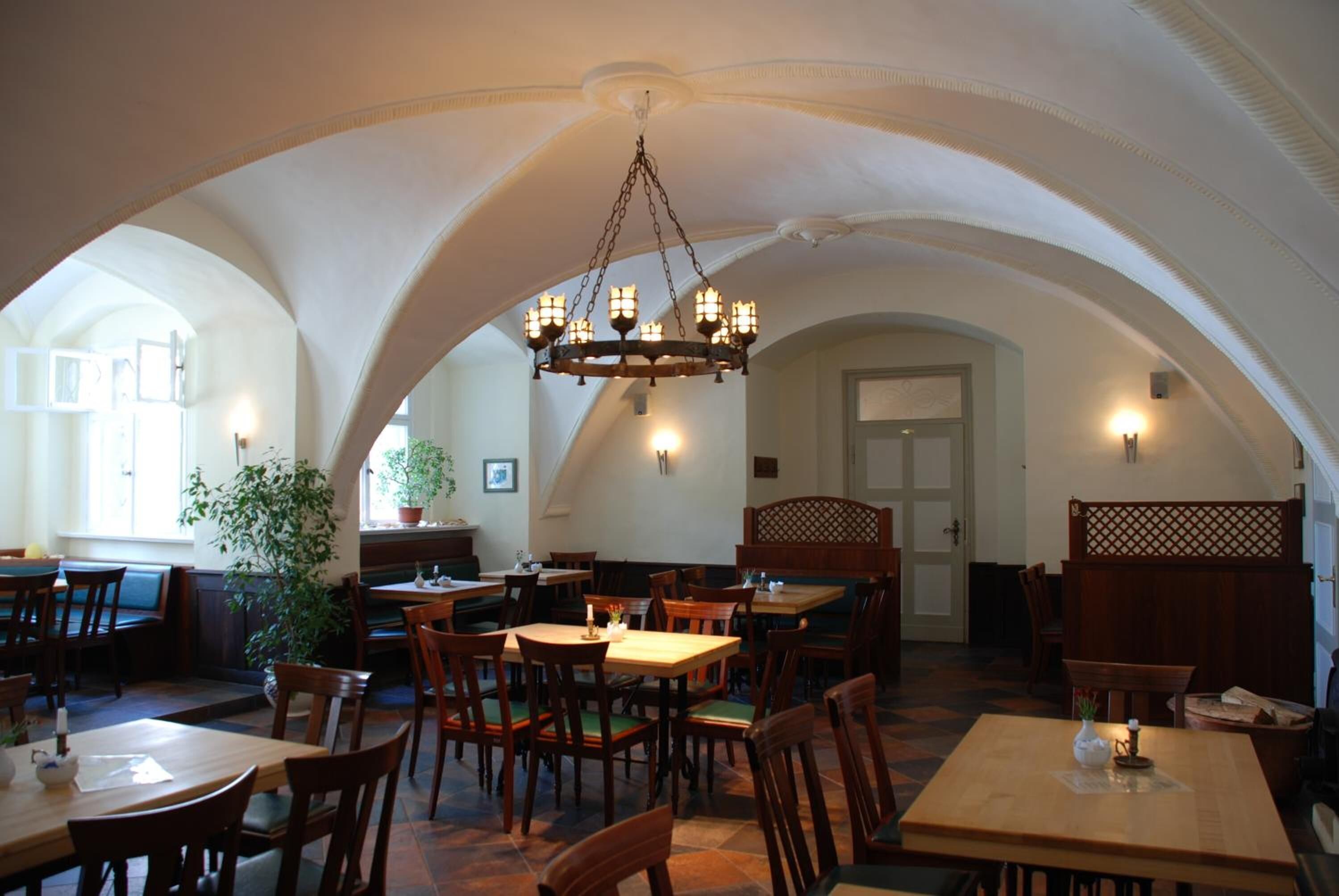 An interior with arched ceilings, wooden tables and chairs, and a chandelier.