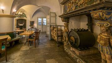 A historic interior with a stone floor, wooden furniture, a fireplace with a large barrel, and ornate carvings.