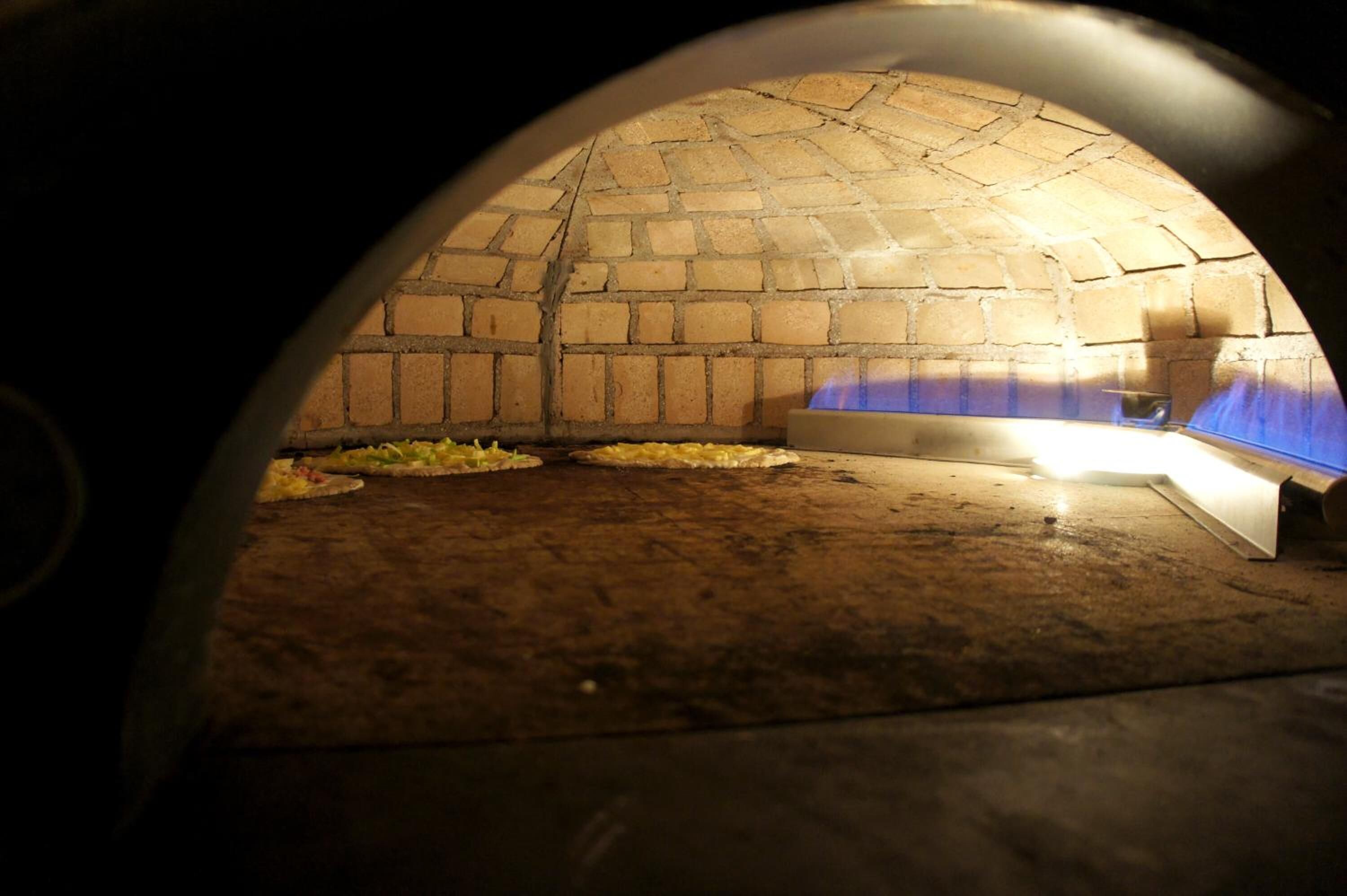 An indoor brick oven with a fire burning inside, surrounded by a dark interior.