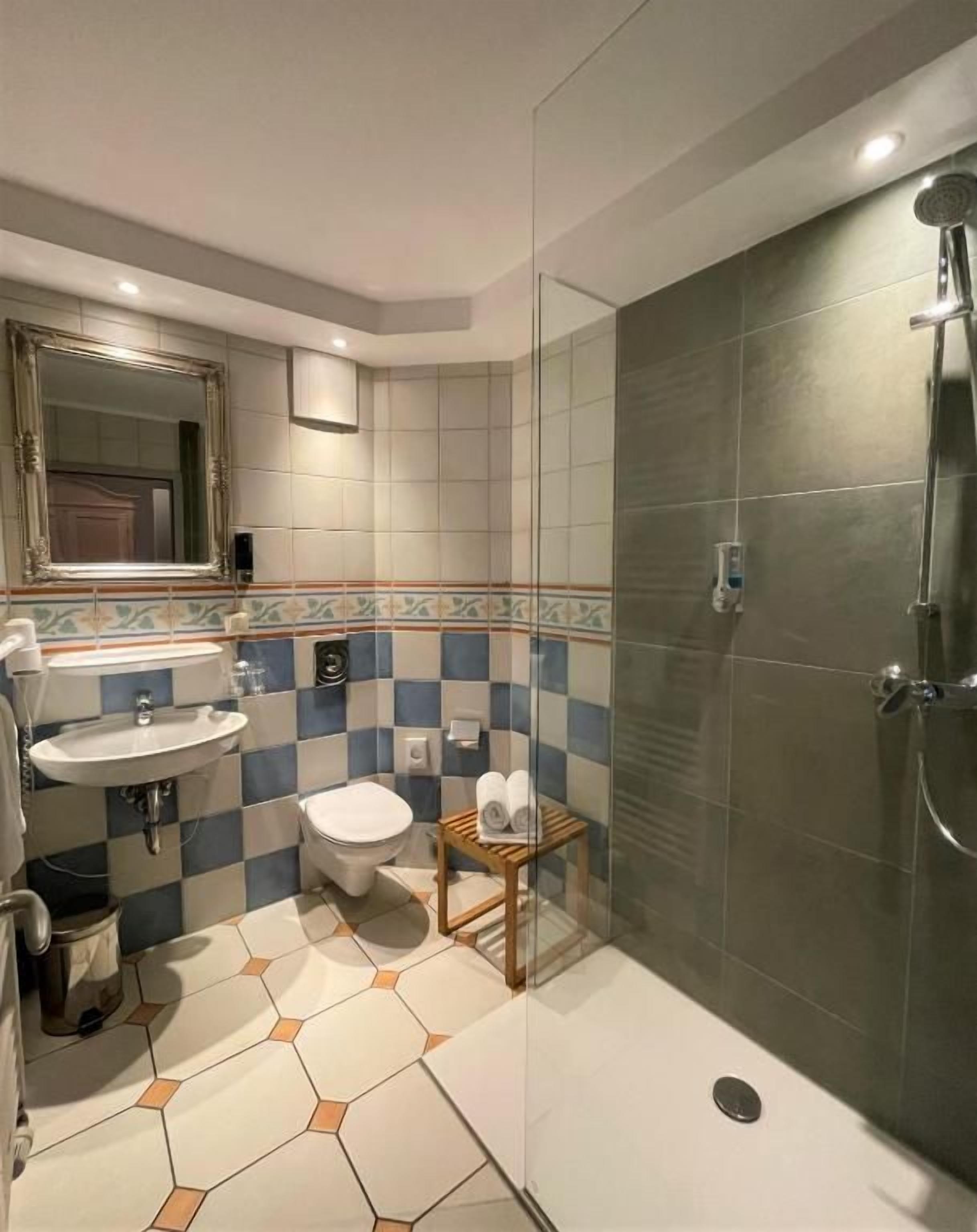 Une salle de bain avec une douche à parois de verre, un lavabo, des toilettes et un petit tabouret en bois.