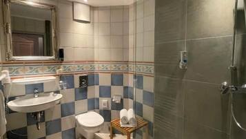 Une salle de bain avec une douche à parois de verre, un lavabo, des toilettes et un petit tabouret en bois.