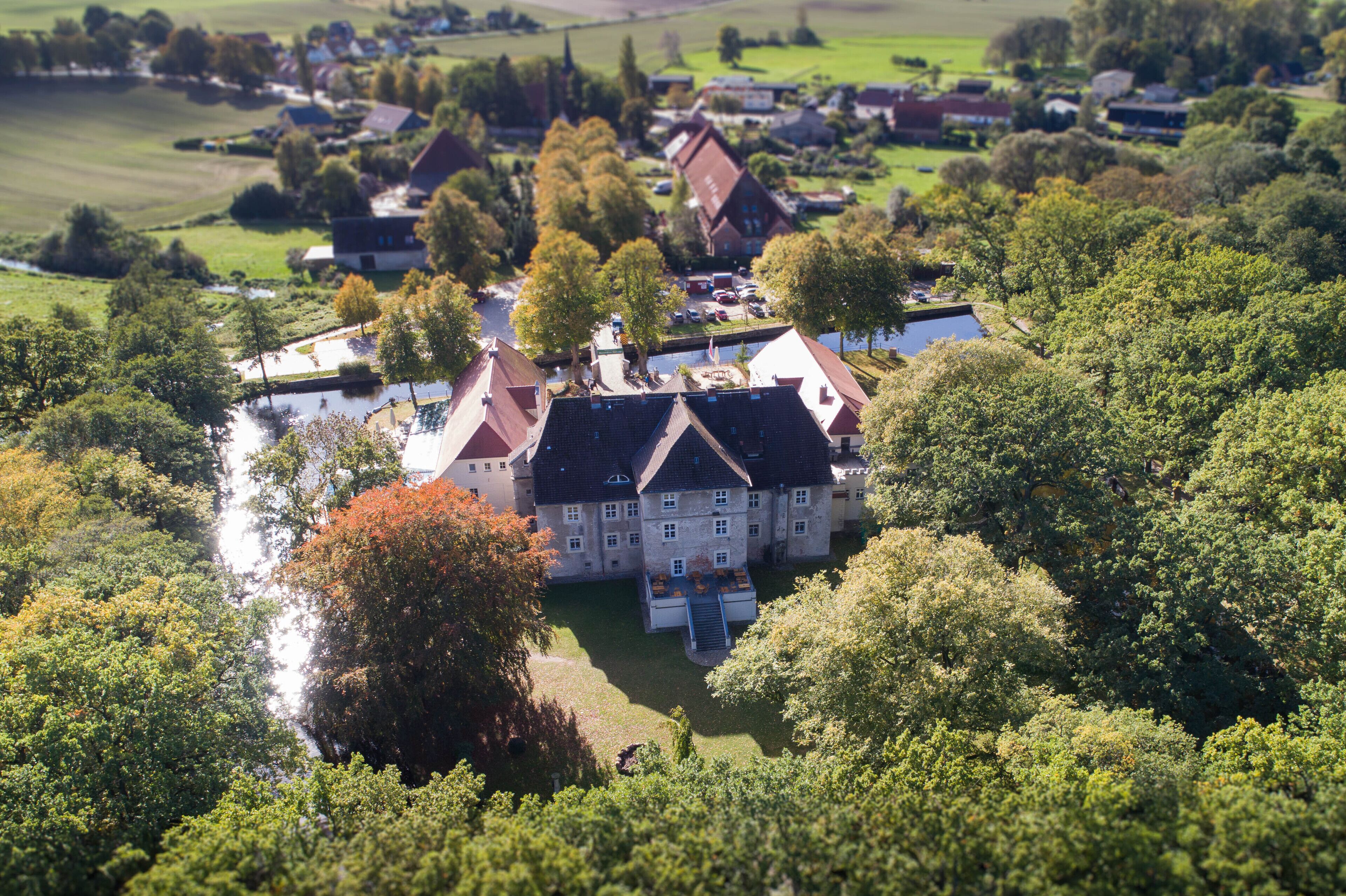 An aerial view of a large estate with multiple buildings, surrounded by lush greenery and a small body of water.