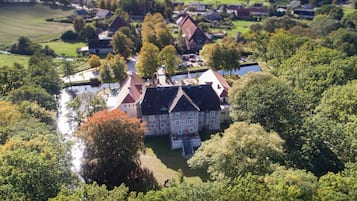 An aerial view of a large estate with multiple buildings, surrounded by lush greenery and a small body of water.