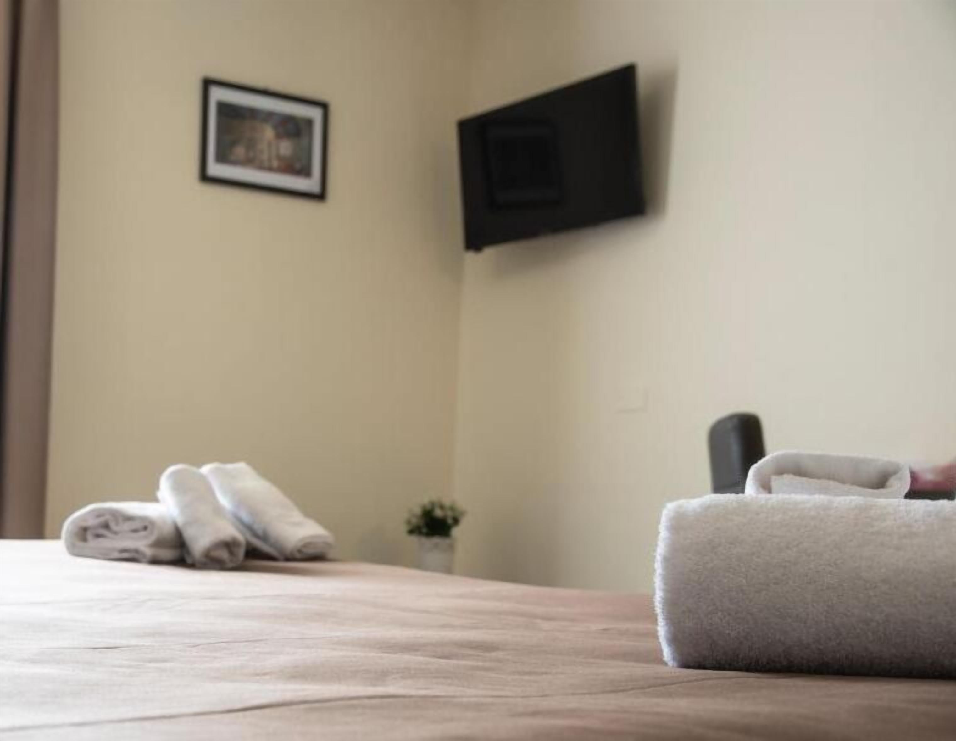 Ein ordentlich bezogenes Bett mit gefalteten Handtüchern, einer kleinen Topfpflanze und einem gerahmten Bild an der Wand.