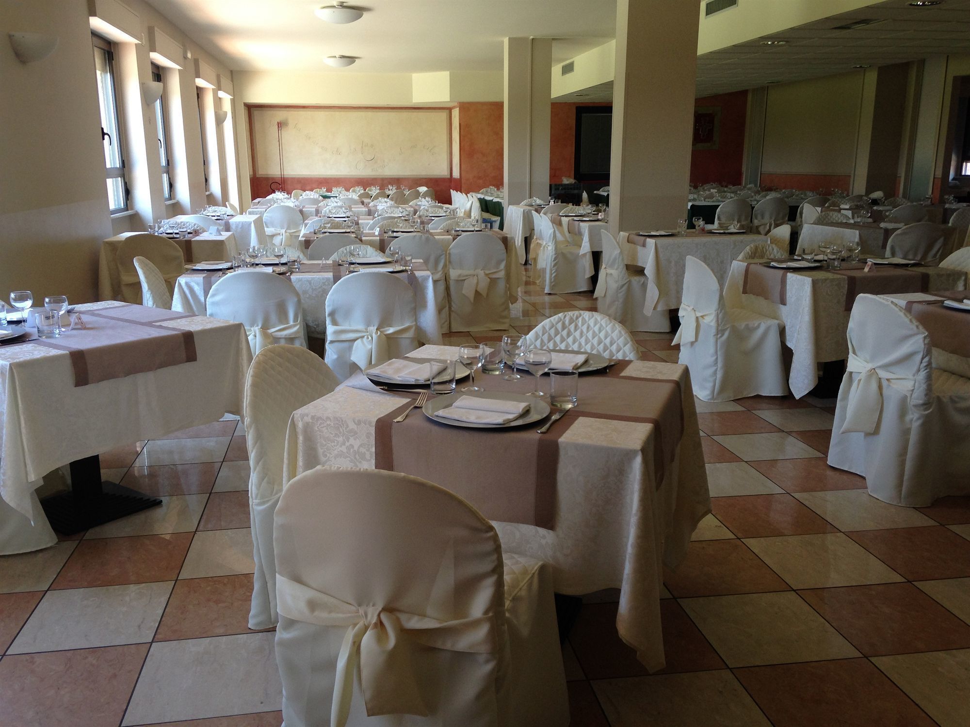 A banquet hall with tables set for a formal event, featuring white tablecloths and chairs with white sashes.