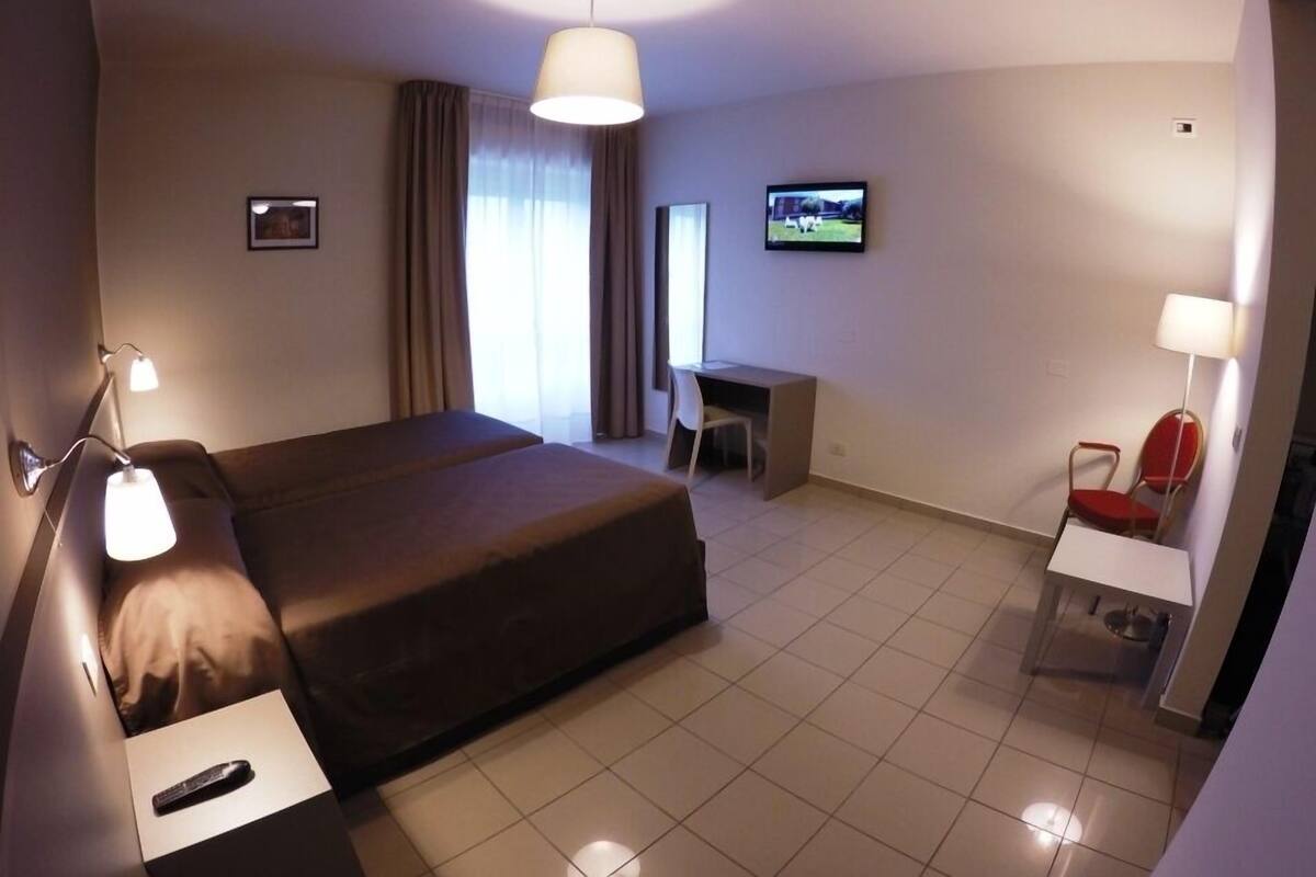 Habitación de hotel con cama, escritorio, silla, televisor y dos lámparas.
