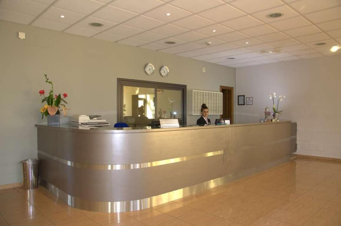 A reception desk with a receptionist, a clock, and a trash can.