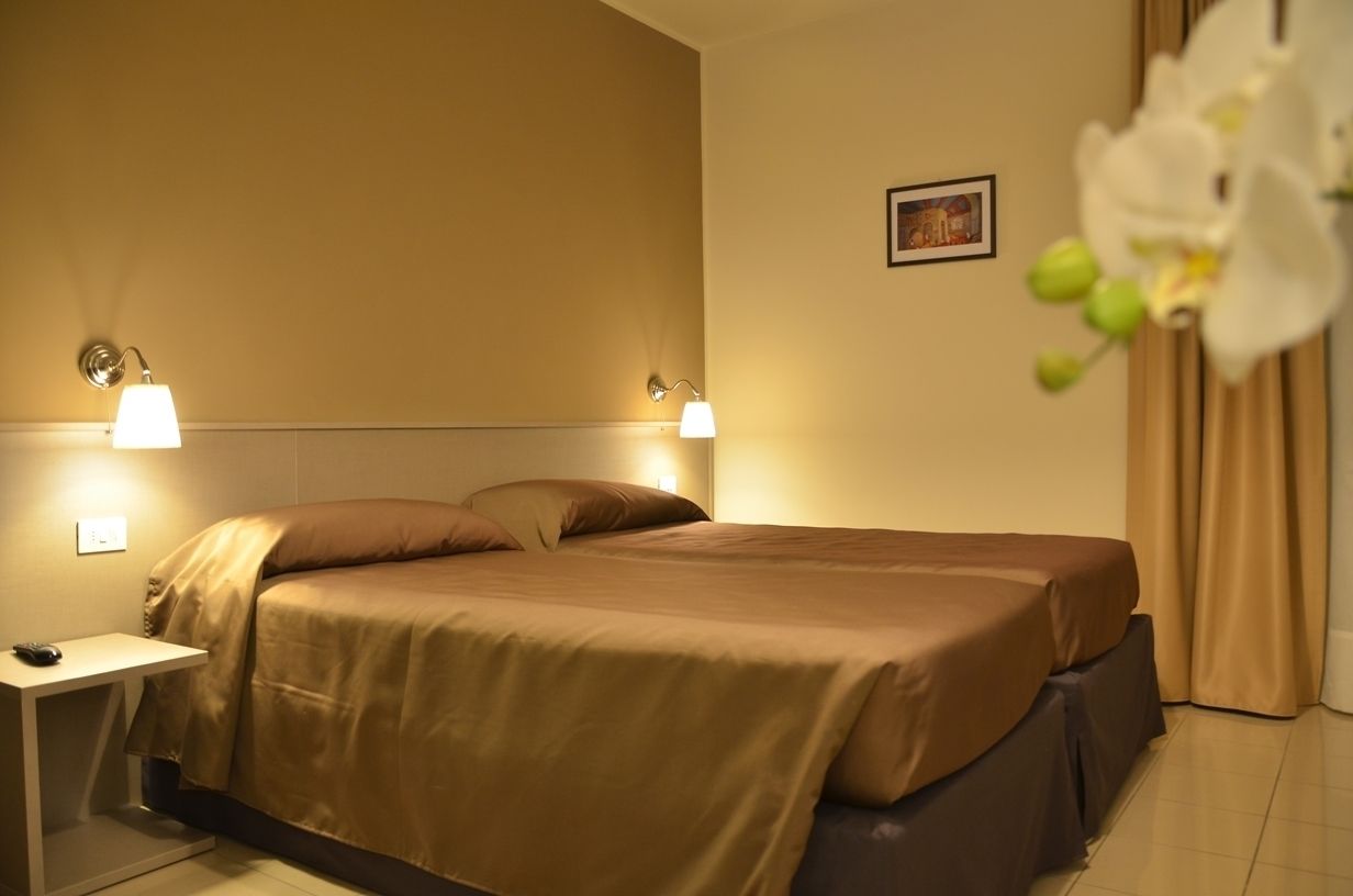 A hotel room with a bed, two bedside lamps, a nightstand, and a picture on the wall.