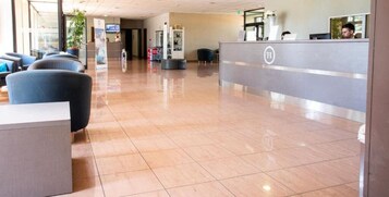 Zona de recepción de un hotel con piso de baldosas brillantes, un mostrador de recepción y áreas de descanso.