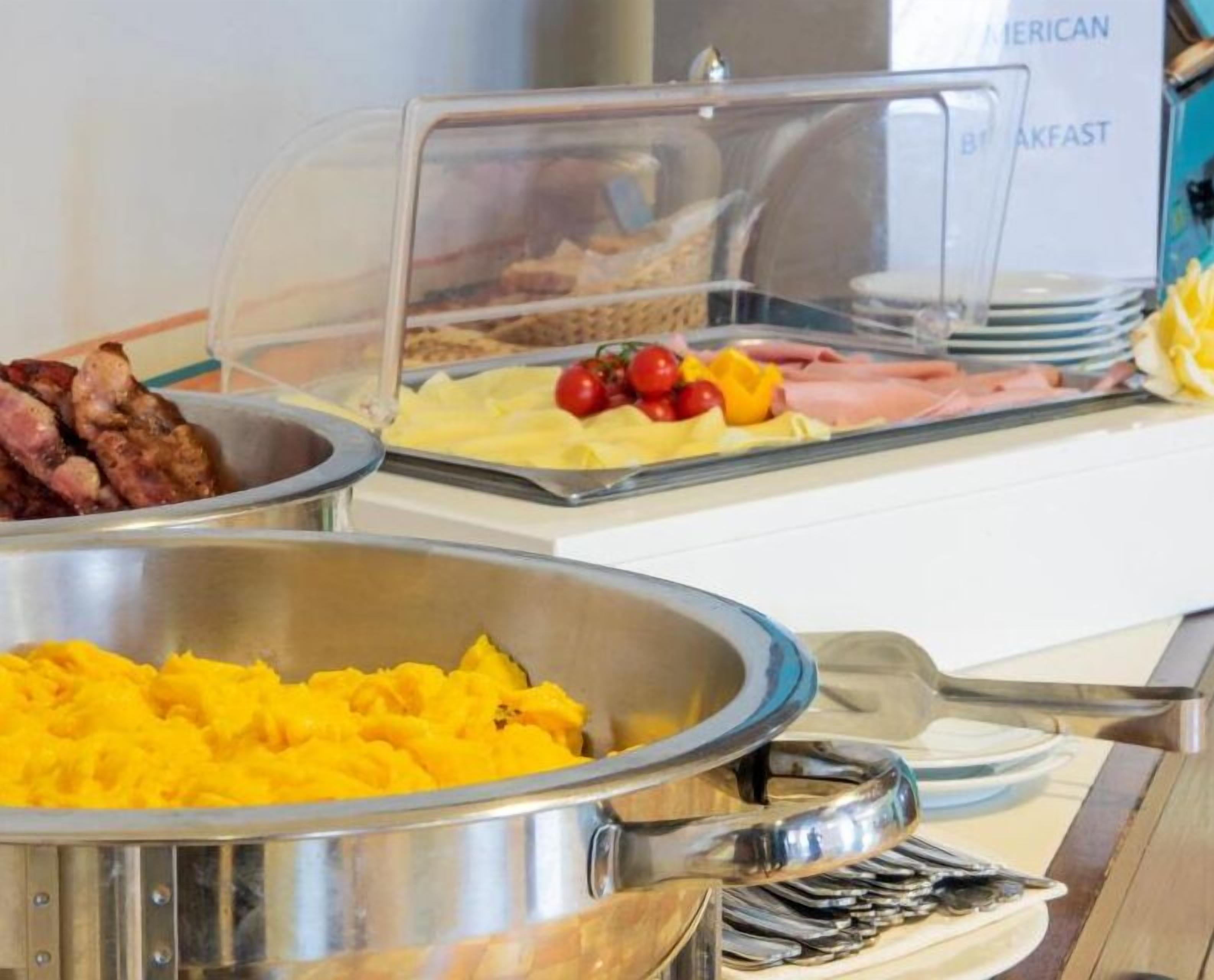 Ein Buffet mit verschiedenen Speisen, darunter Rührei, Speck und gelbe Früchte.