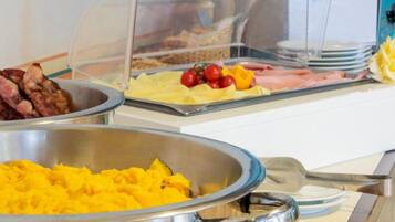 Ein Buffet mit verschiedenen Speisen, darunter Rührei, Speck und gelbe Früchte.