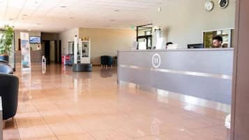 Uma área de recepção de hotel com design moderno, apresentando um balcão de atendimento, área de estar com cadeiras e piso revestido de azulejos.
