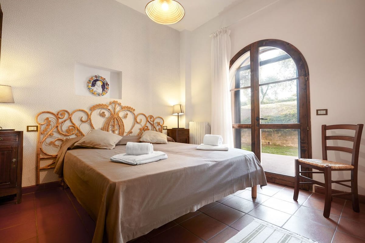 Une chambre à coucher avec un grand lit, une tête de lit en bois, une fenêtre avec des rideaux et une chaise.