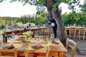 Een restaurant met buitentafels en stoelen, een grote boomstam en hangende lantaarns.