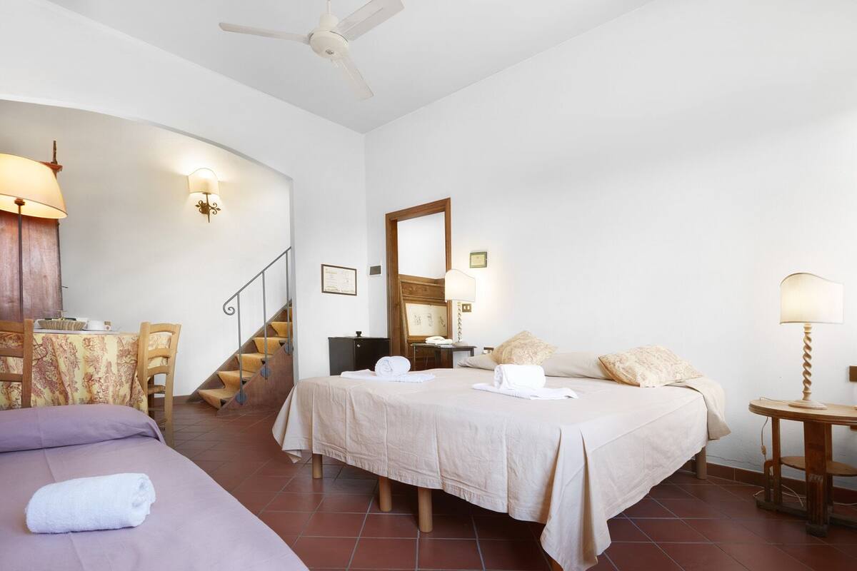 Une chambre d’hôtel comprenant un lit, un bureau, une chaise, une petite table, une lampe, un miroir et un escalier.