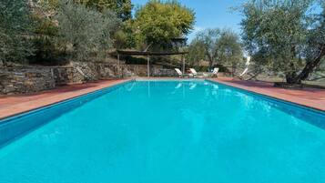 Una piscina rettangolare con acqua cristallina, circondata da muri in pietra e alberi.