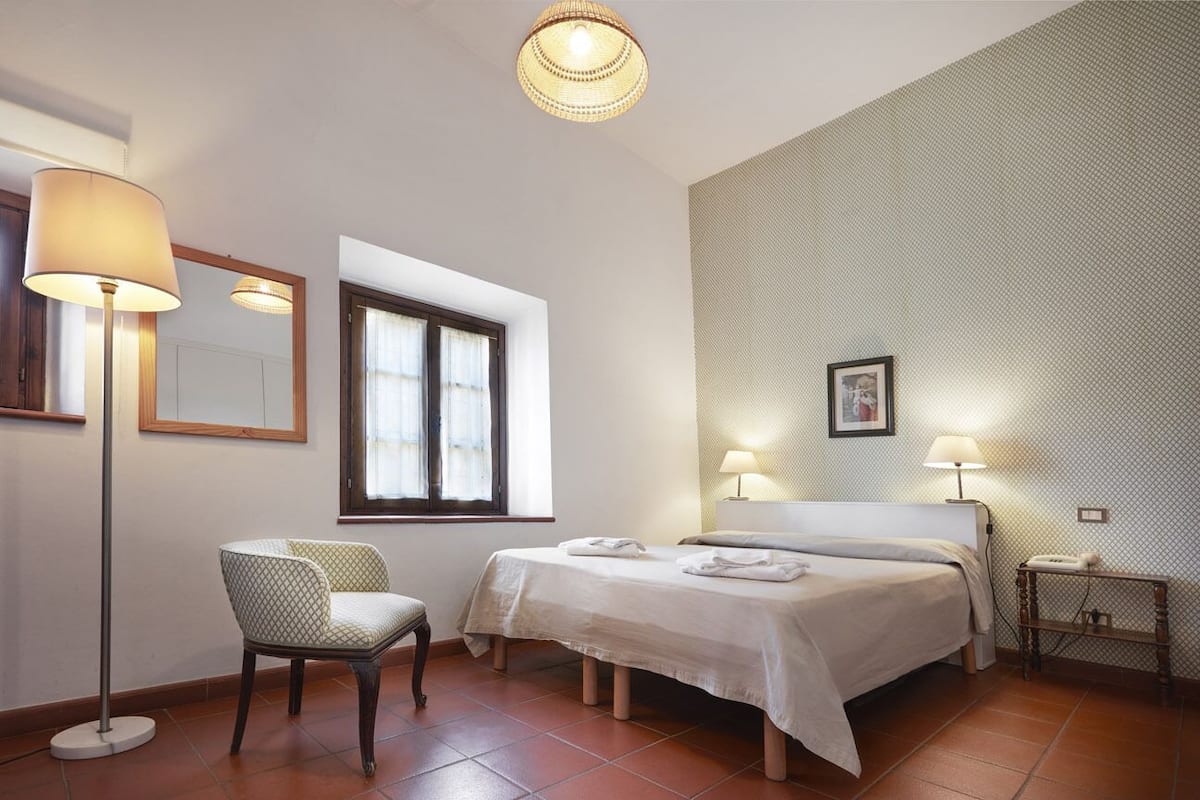 Une chambre d’hôtel avec deux lits, une chaise, une lampe sur pied et une fenêtre.