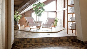 A cozy indoor seating area with two white cushioned chairs, a wooden bench, and a potted plant. - Berghotel Trübsee (Engelberg)