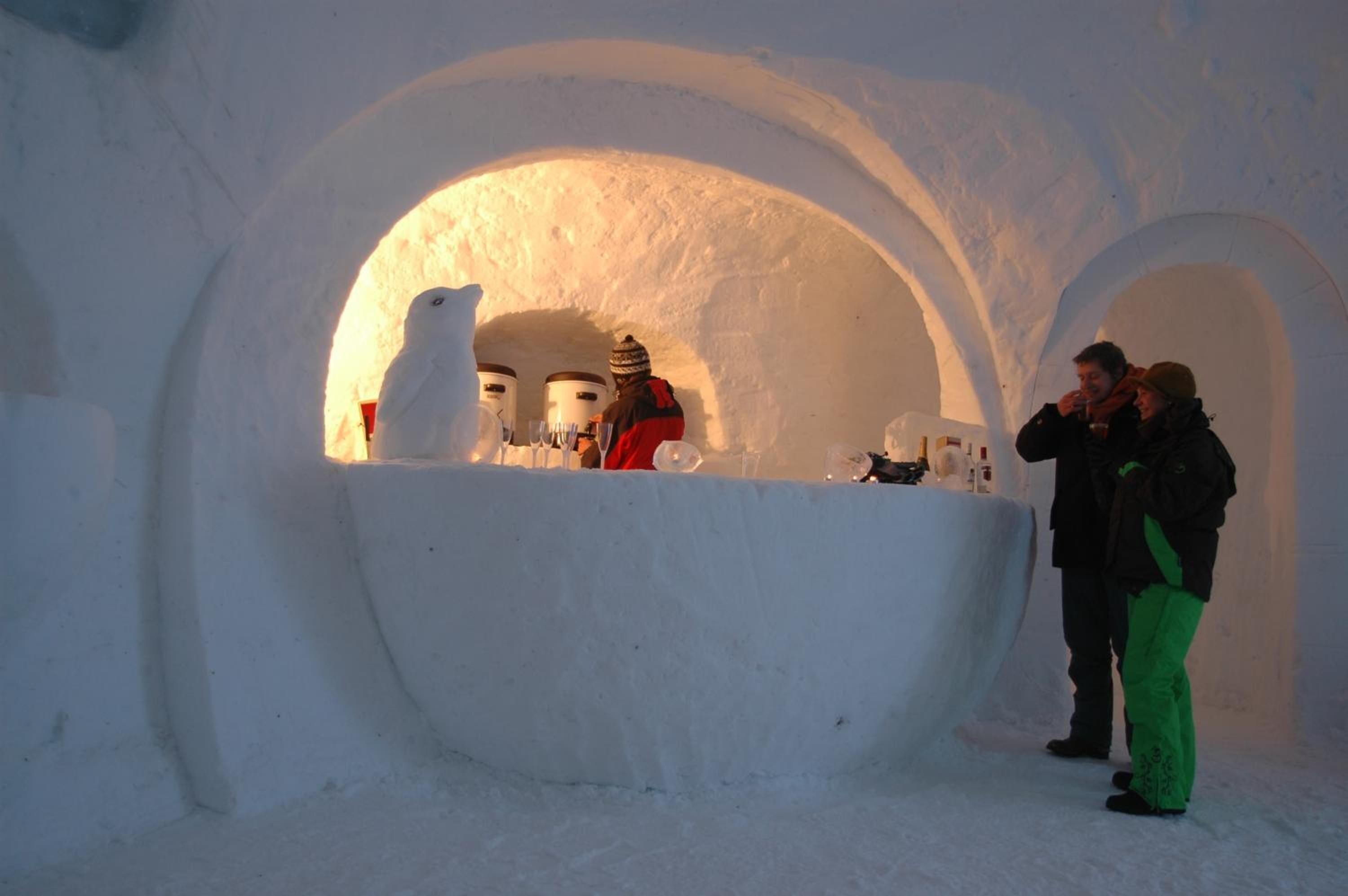 An igloo with a central seating area and two people standing outside.