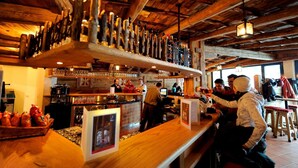 A rustic bar area with wooden beams, a variety of bottles, glasses, and a coffee machine. - Berghotel Trübsee (Engelberg)