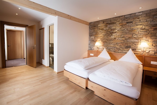A bedroom with two beds, wooden flooring, a stone wall, and a wooden ceiling beam.