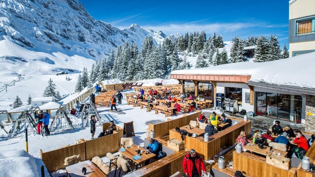 A snow-covered outdoor dining area with wooden tables and benches, surrounded by snow-covered trees and mountains. - Berghotel Trübsee (Engelberg)