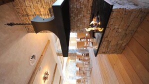 A modern interior with a stone wall, a fireplace, and a seating area with wooden chairs. - Berghotel Trübsee (Engelberg)
