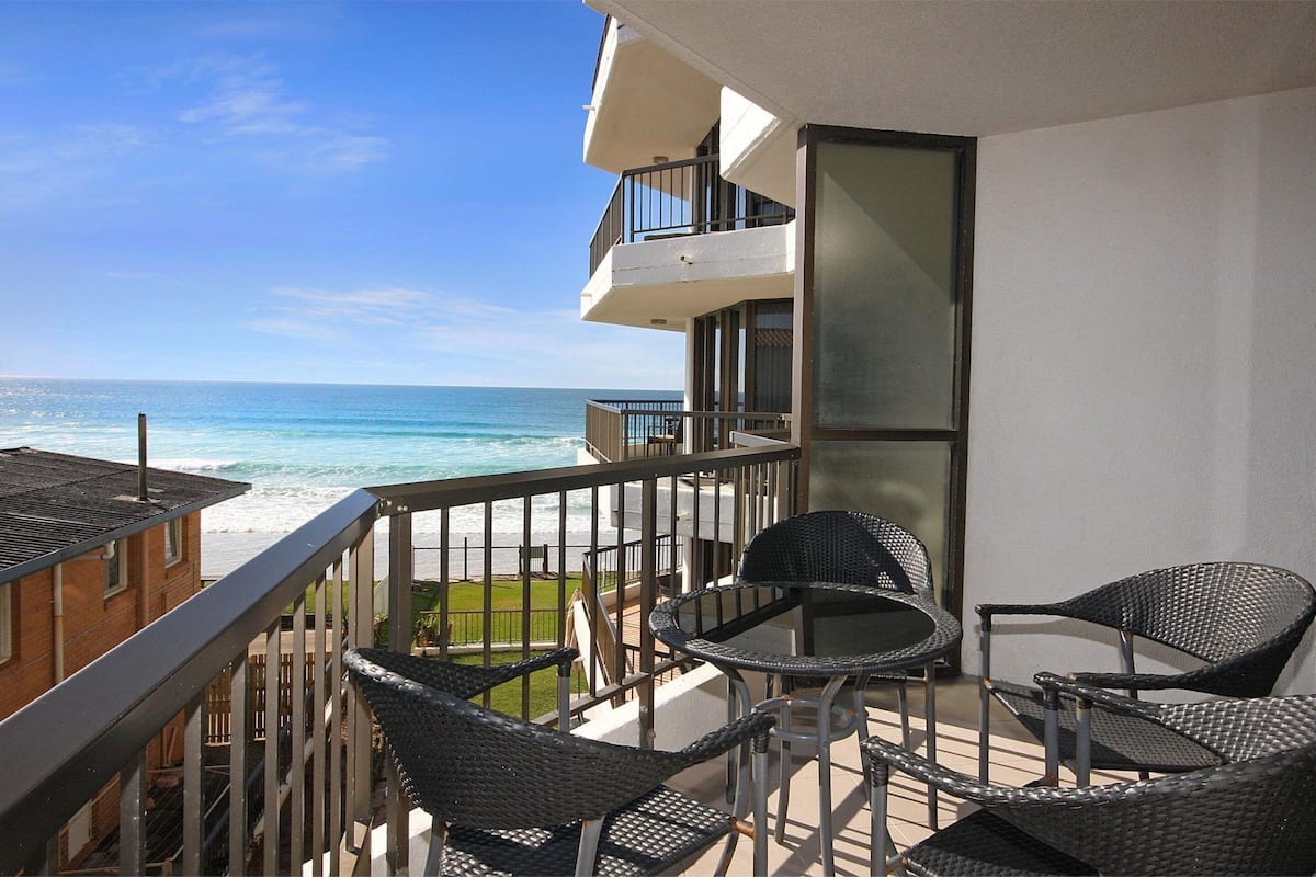 A balcony with wicker chairs and a table overlooking the ocean.