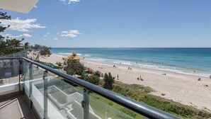 Vista a la playa desde un balcón con barandillas de vidrio, una playa de arena y el océano.