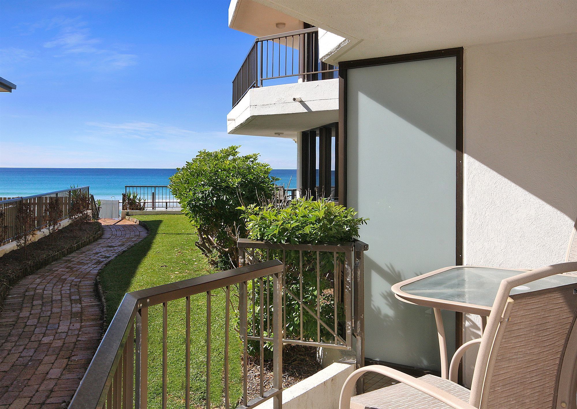 A balcony with a view of the ocean, a small garden, and a table with chairs.