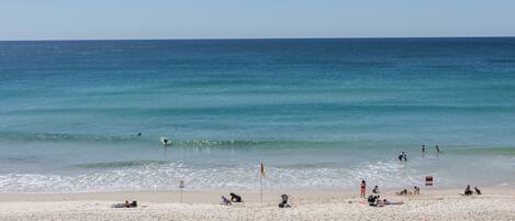 A beach with people sunbathing and swimming, clear skies, and calm sea.