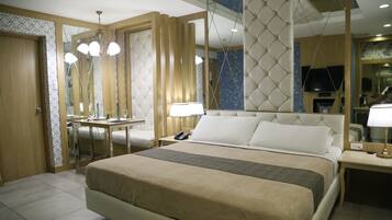 A hotel room with a large bed, bedside tables, a desk with a chair, a mirror, and a television.