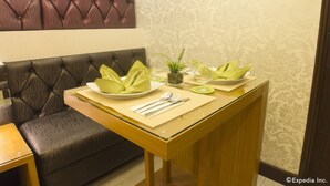 Un coin repas avec une table dressée pour deux personnes, un banc rembourré et un mur décoratif.