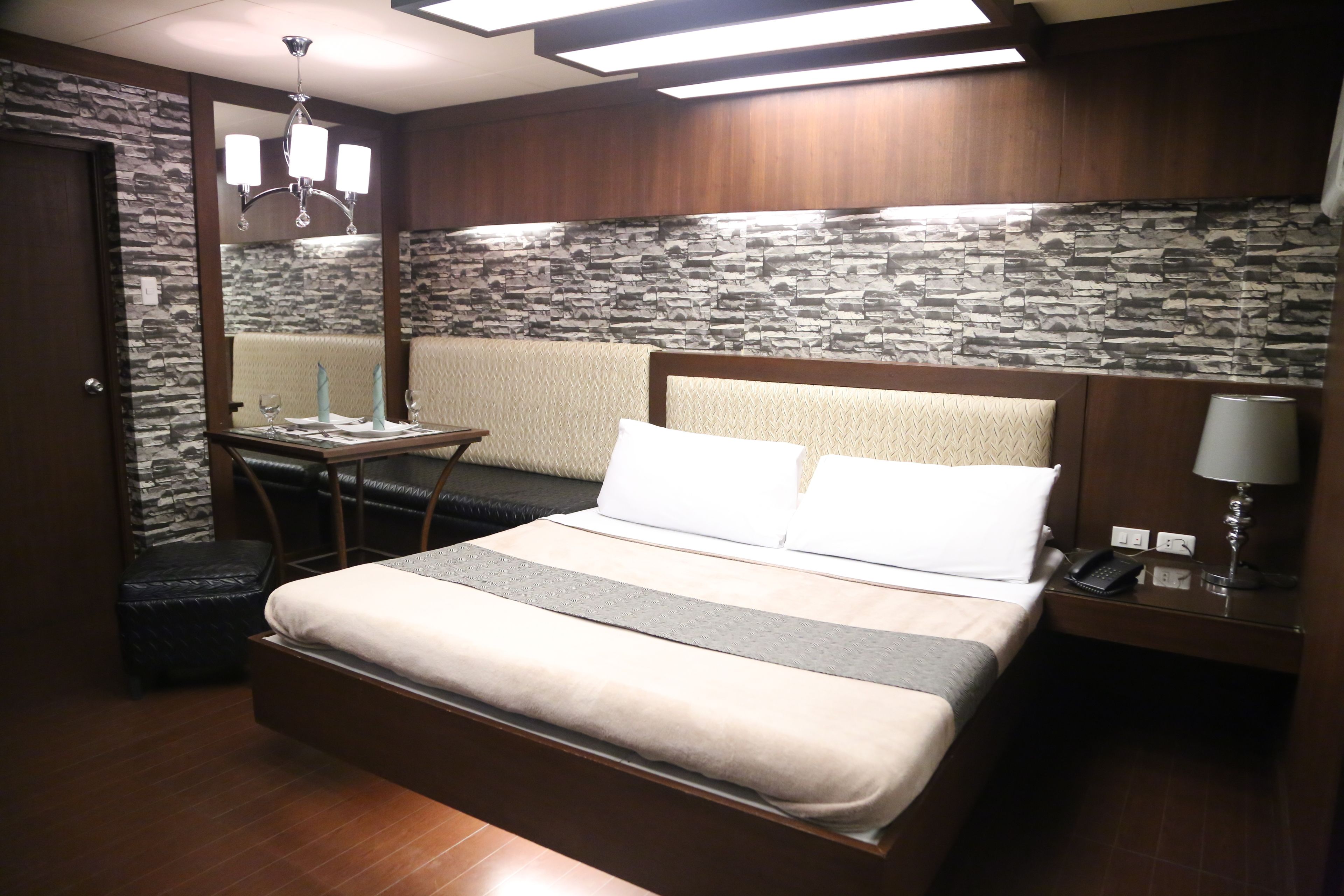 A hotel room with a bed, bedside table, lamp, and a small table with a chair.
