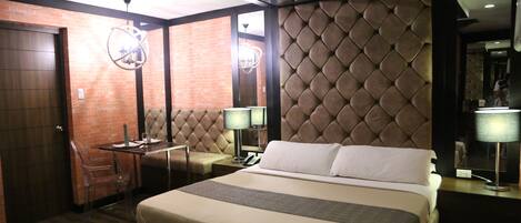Habitación de hotel con una cama grande, un escritorio con silla, una mesita y un diseño de pared en patrón de diamantes.