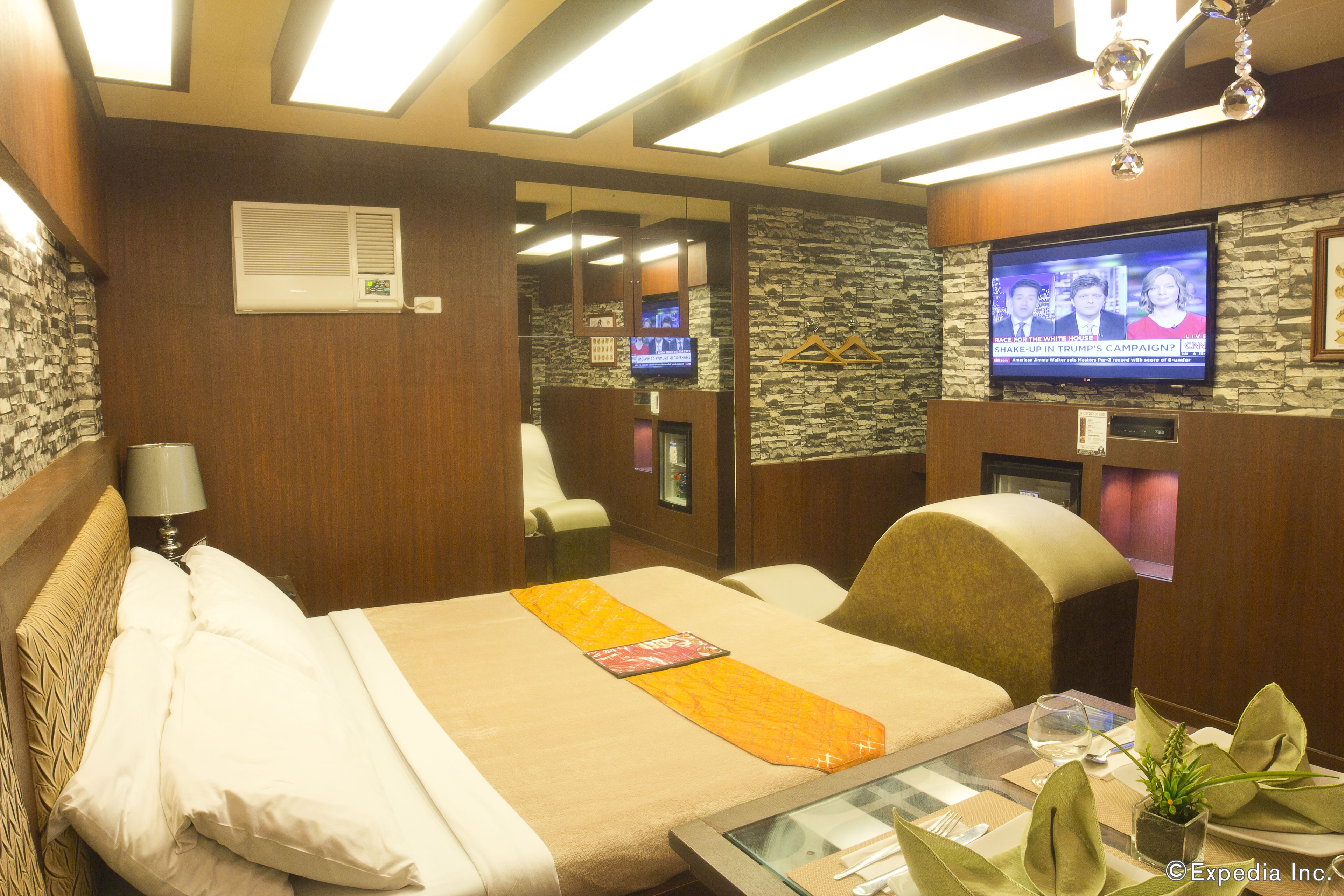 A hotel room with a bed, a television, a mirror, and a small table with a plant and a glass of water.