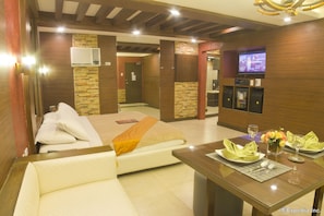 A hotel room with a bed, a sofa, a dining table set with plates, glasses, and a vase of flowers.