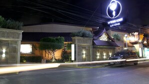 L’entrée d’un hôtel, avec une enseigne lumineuse au néon, une voiture garée devant et une façade bien éclairée.
