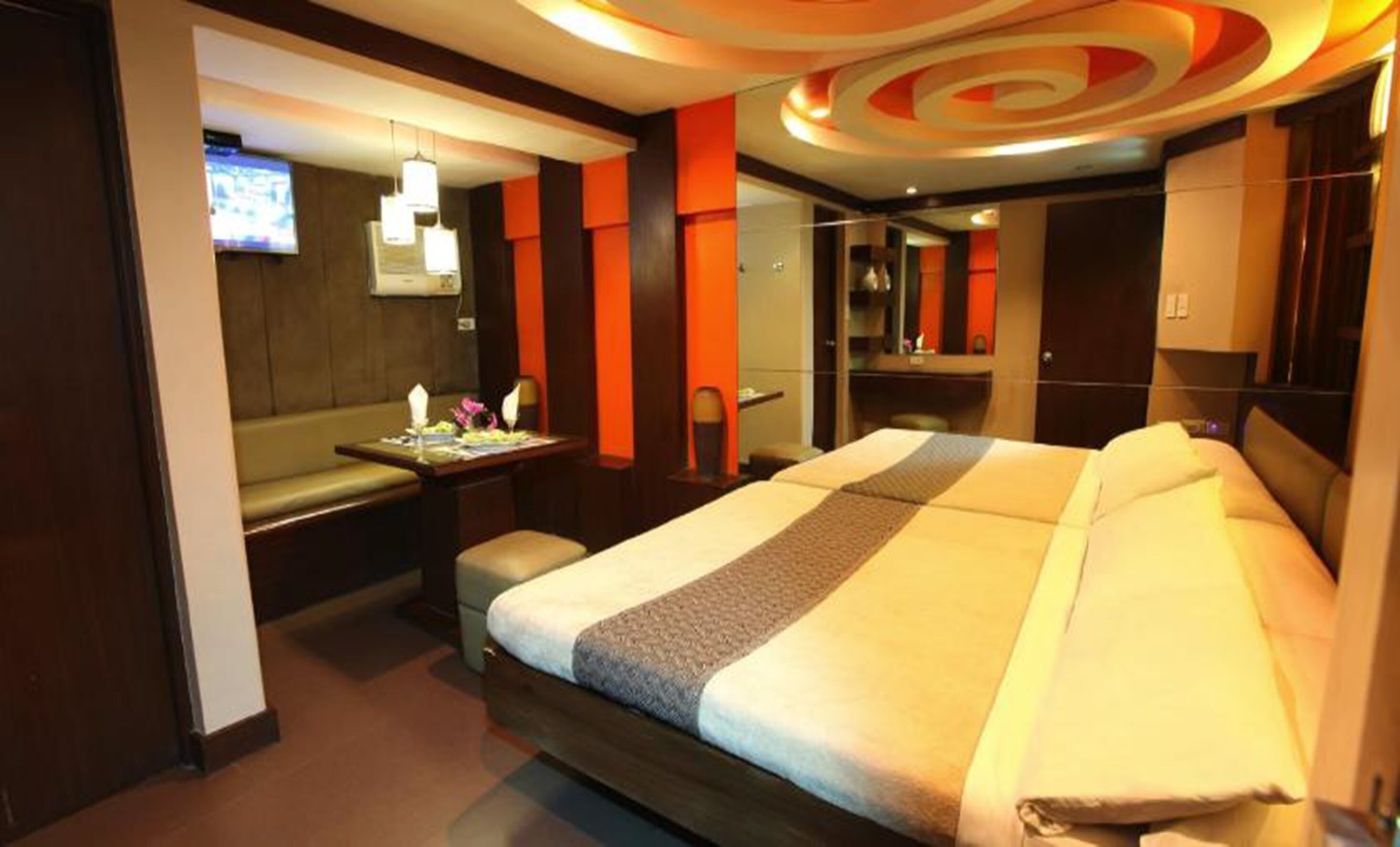 A hotel room with a large bed, a desk with a chair, a small seating area, and a TV on the wall.