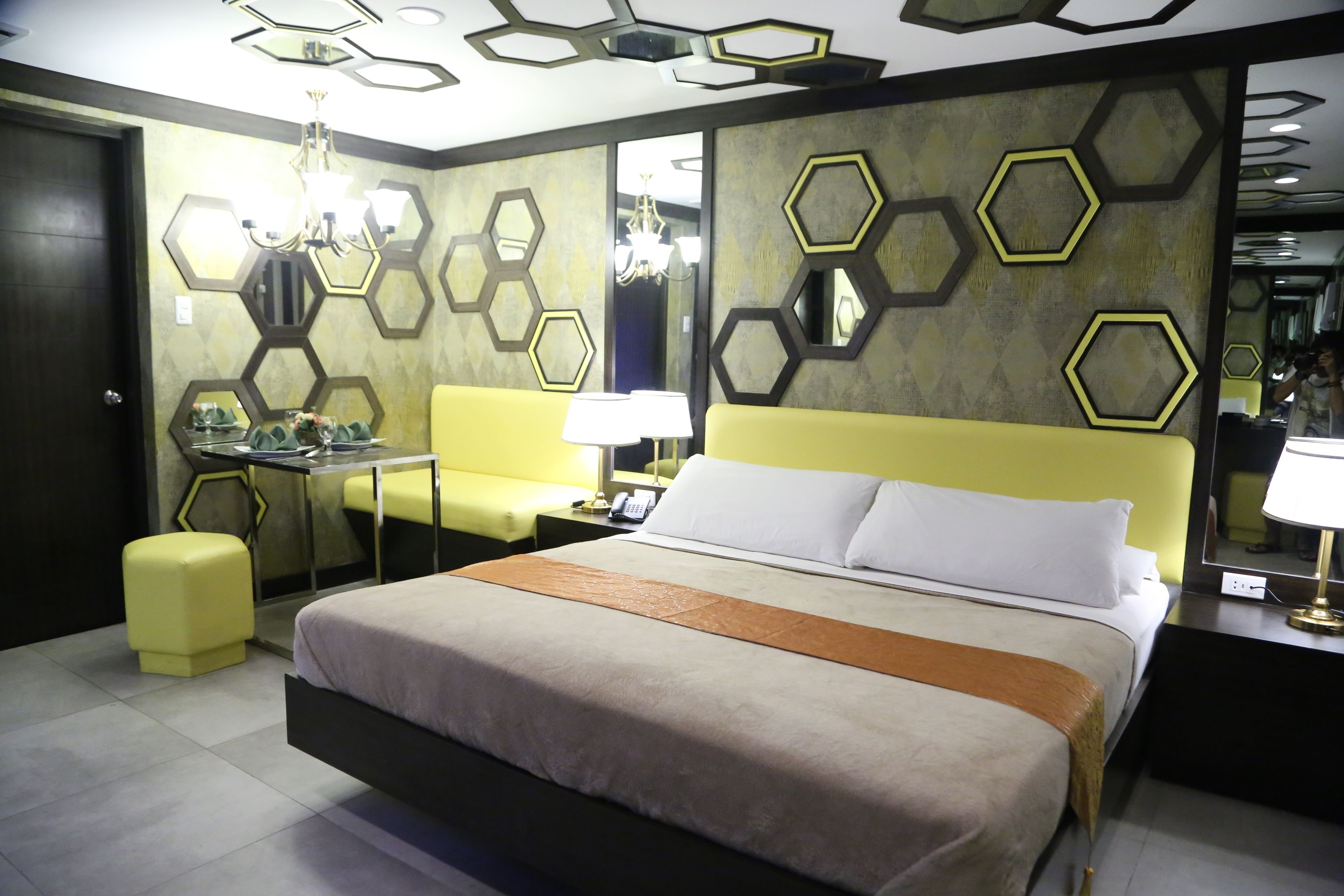 A modern hotel room with a large bed, a desk, a chair, and a mirror.